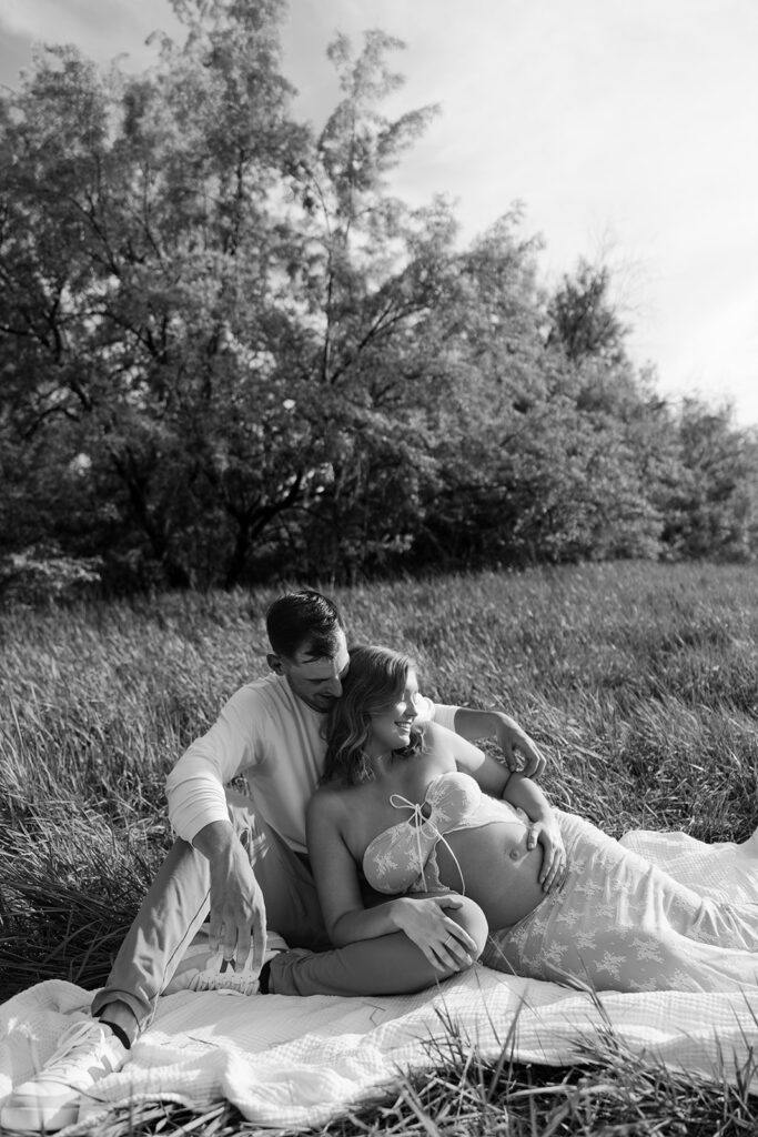 Man and pregnant woman lay together in a grass field on a picnic blanket