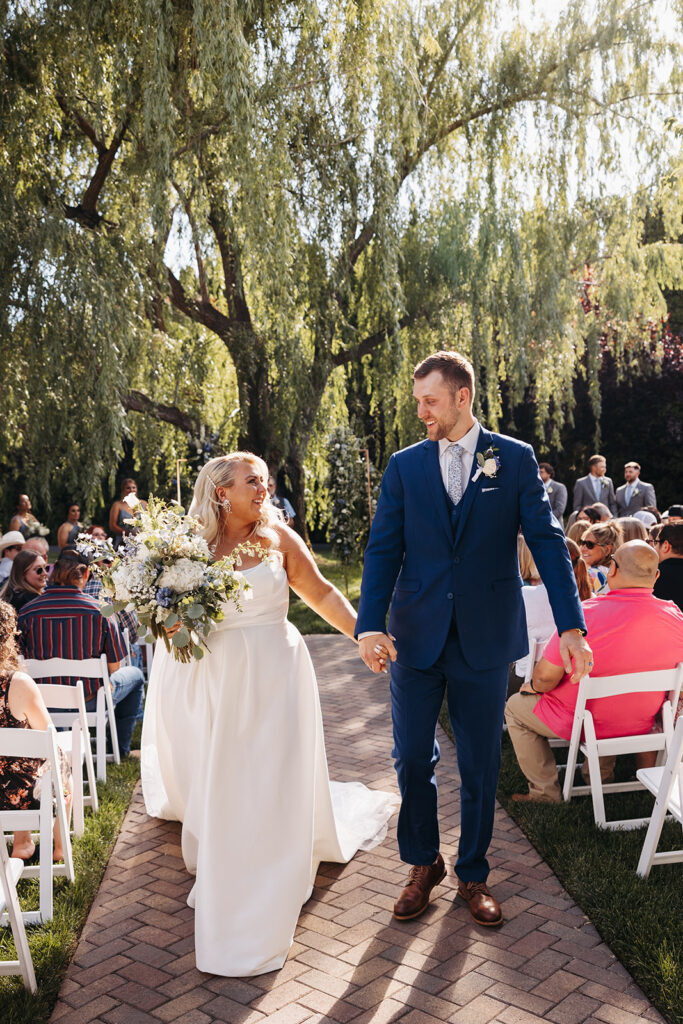 The couple walking hand-in-hand through the Promise Garden, framed by vibrant flowers.