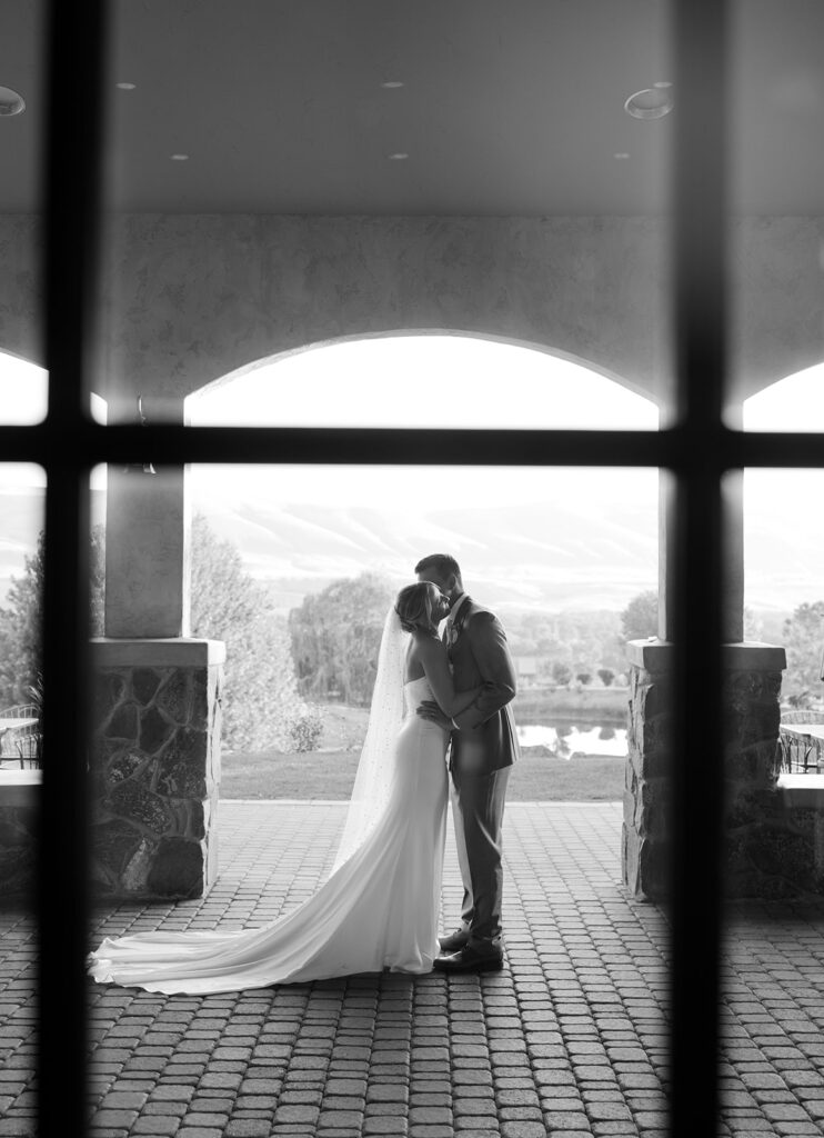 Bride and groom captured through a window as they embrace.