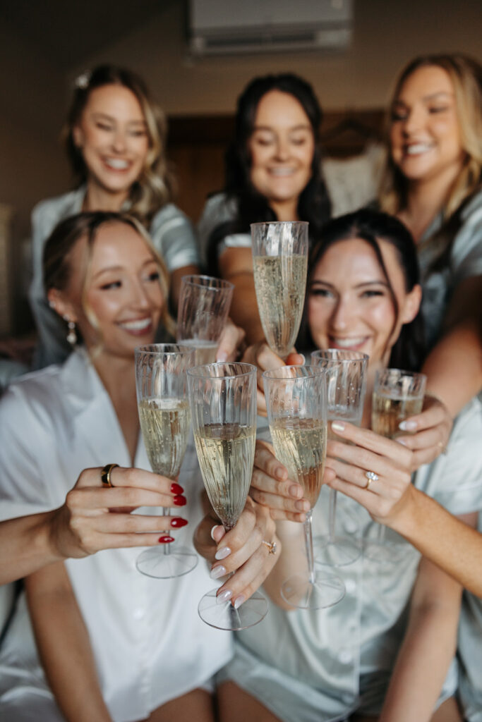 Bride and bridesmaids toast with champagne in their getting ready outfits before the ceremony.