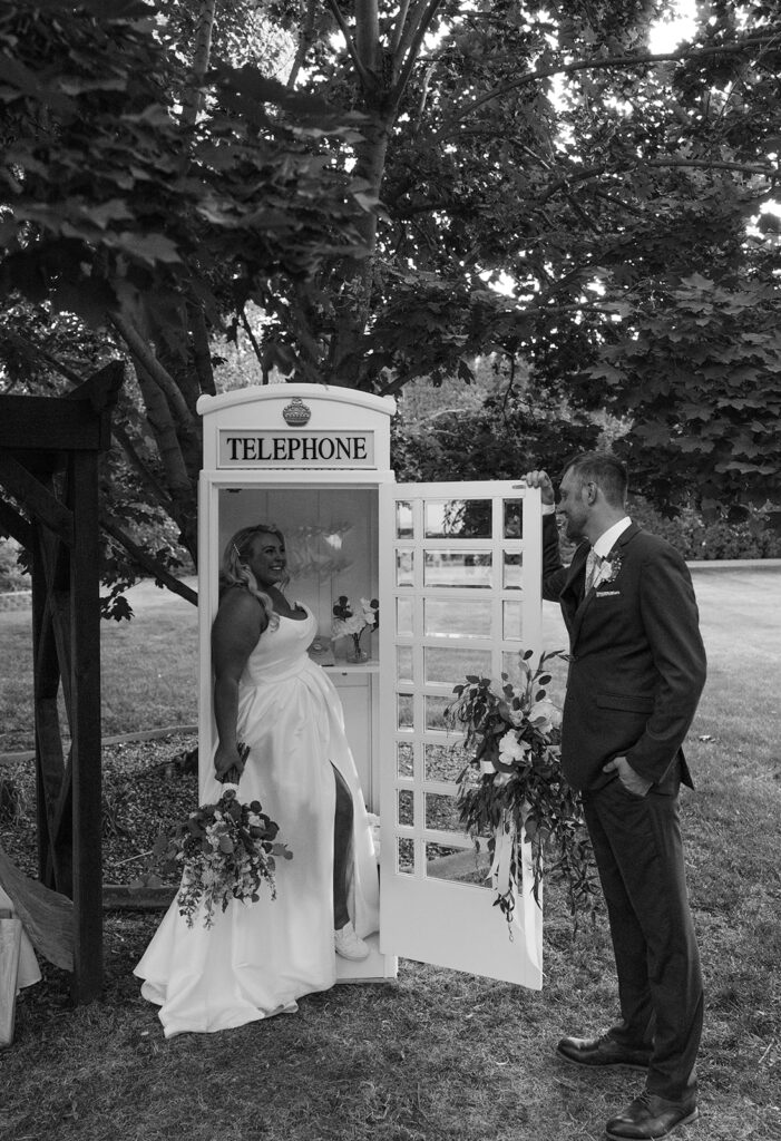 Samantha and Austin stand playfully in a white telephone booth