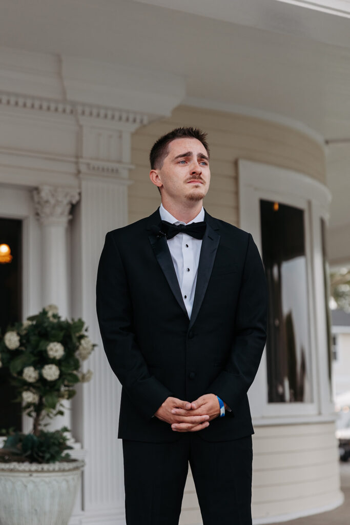 Groom waits on the front porch of The Moore Mansion as his bride walks down the aisle