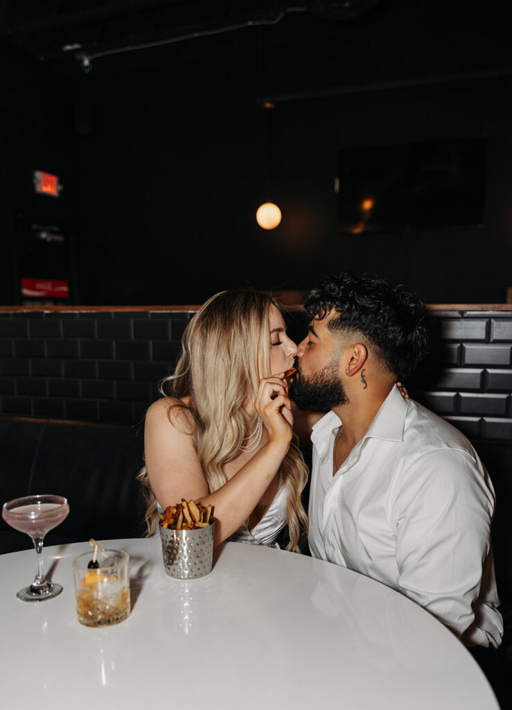 Couple sits playfully in a bar booth during their engagement photo session