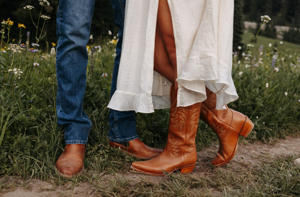 Close up of couples cowboy boots with wildflowers in the backdrop during their couples photo session