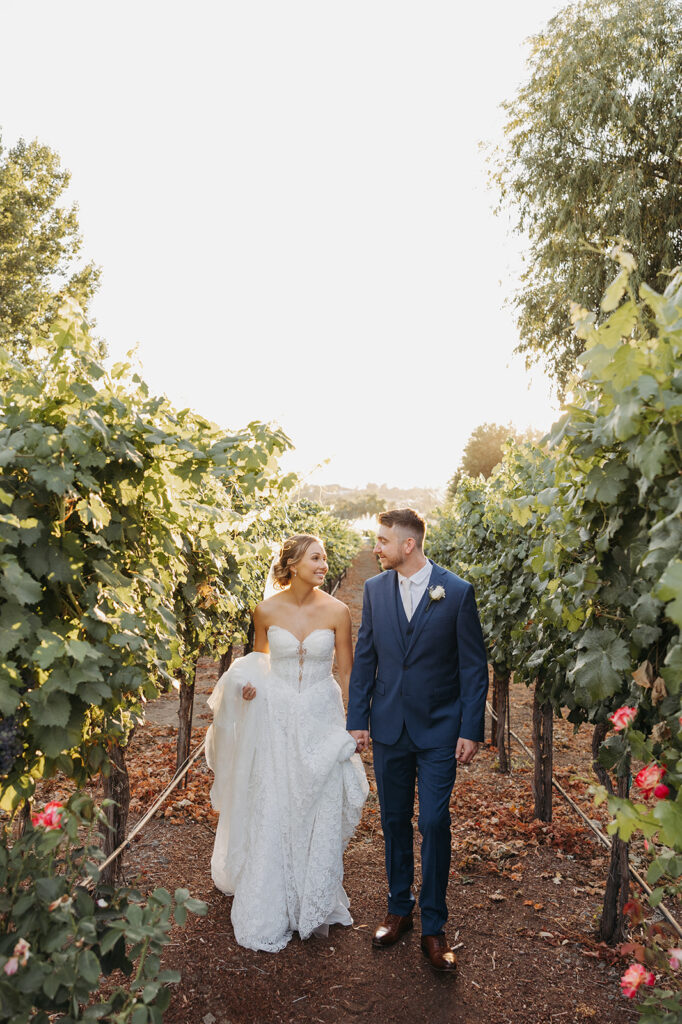 Bride and groom walk through the Sugar Pine Barn vineyard
