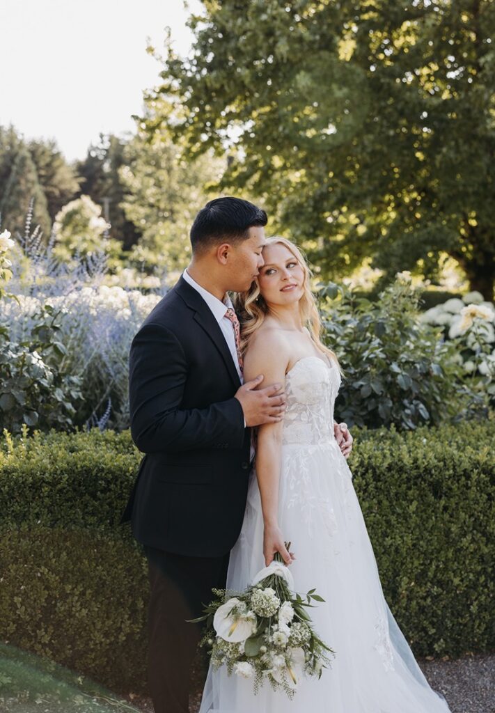 Bride and groom standing together in a garden during golden hour, captured with soft direction in an editorial wedding photography style.