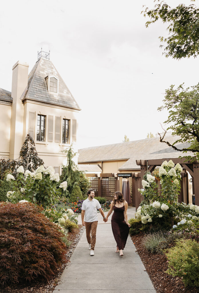 Couple walking hand in hand through a manicured garden courtyard with soft greenery, neutral architecture, and muted floral tones creating a cohesive, elegant color palette.