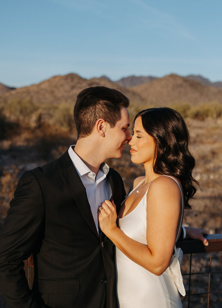 Couple standing close together in the Arizona desert at sunset, sharing a quiet moment with mountains in the background.