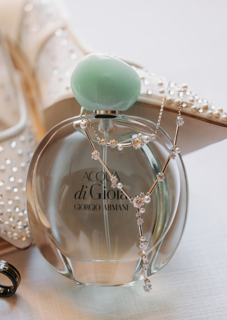 Close-up of Acqua di Gioia by Giorgio Armani perfume bottle styled with a delicate pearl and crystal necklace, photographed alongside embellished bridal heels in soft natural light.