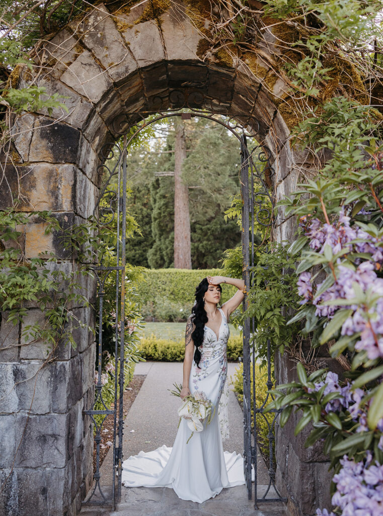 Bride standing beneath a stone garden archway at Chateau de Michellia, surrounded by greenery and soft florals.