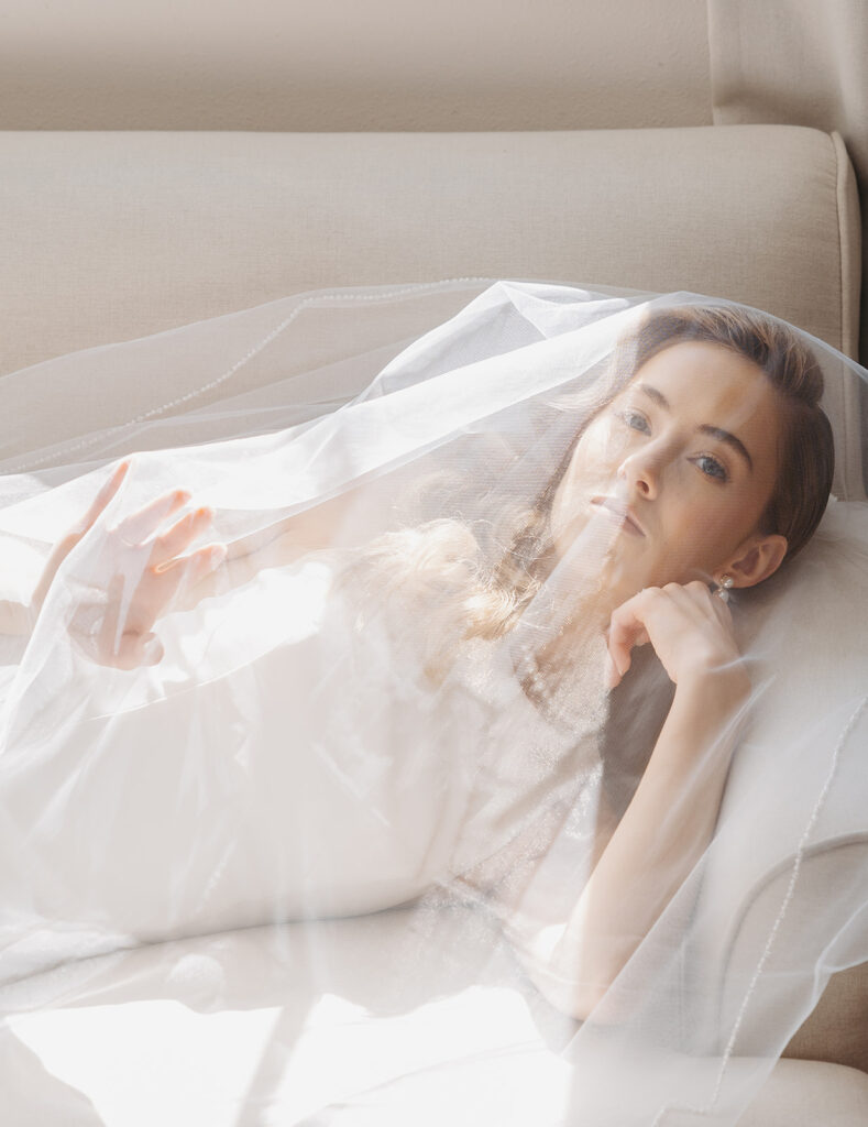 Bride reclining on a sofa with her veil softly draped, photographed in a refined editorial wedding photography style.