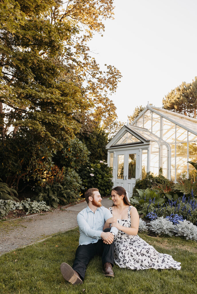 Couple sitting together in a garden near a greenhouse, photographed with an editorial wedding photography perspective.