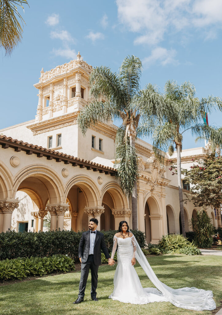 Bride and groom walking hand in hand in front of historic architecture, photographed with an editorial wedding photography approach.