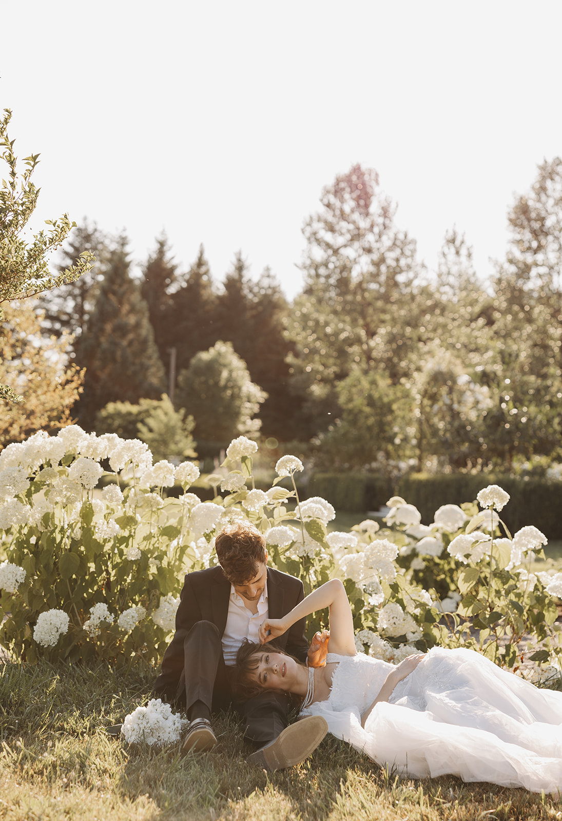 Couple relaxing together in a garden surrounded by white flowers, photographed in a natural and editorial wedding photography style.