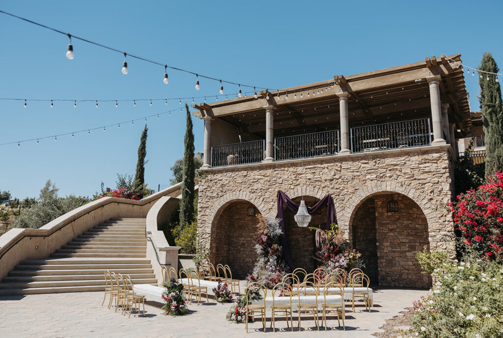 Outdoor wedding ceremony designed by planners in Temecula, California, featuring stone architecture, floral installations, and warm natural light.