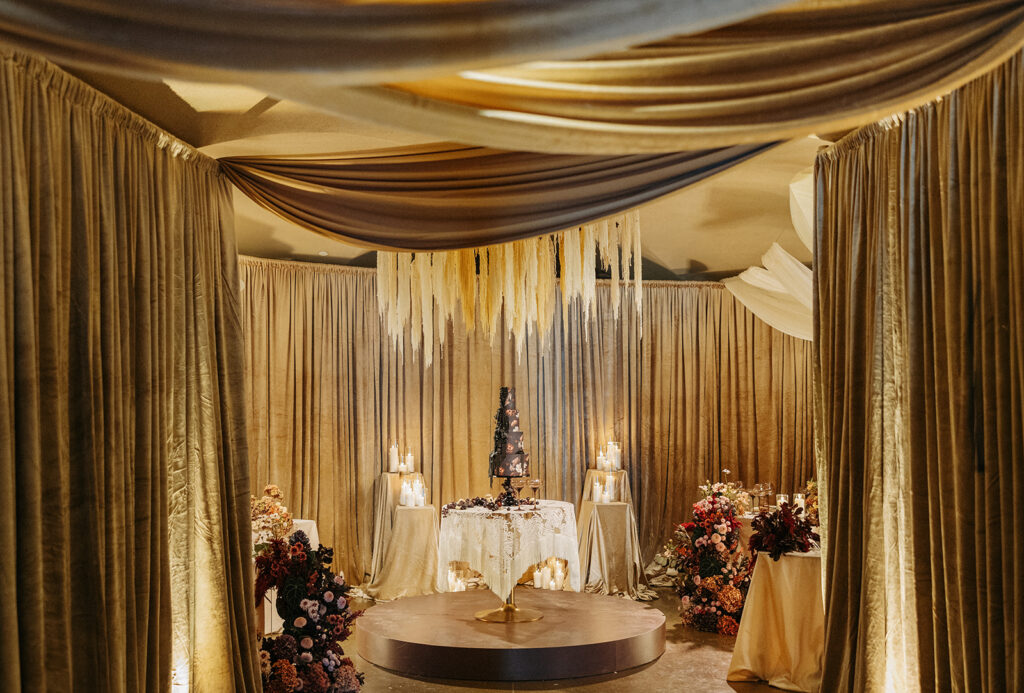 Moody wedding reception design in Temecula, California, featuring layered draping, candlelight, floral installations, and a sculptural cake display.