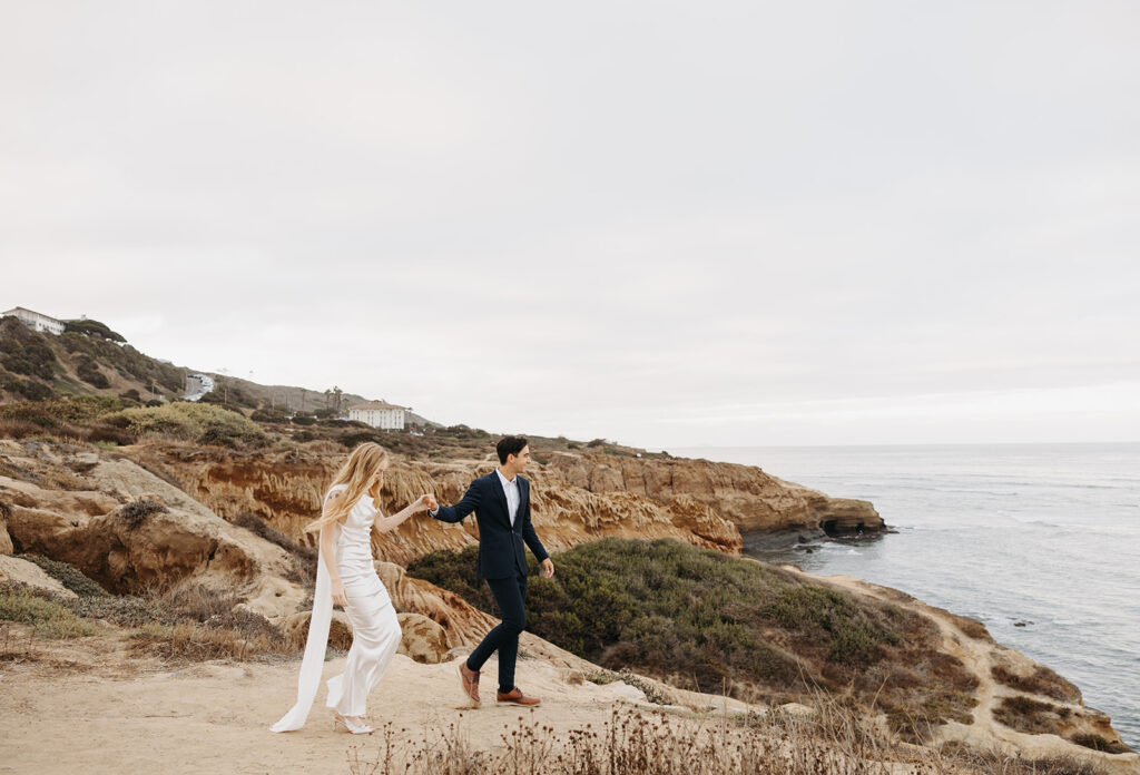 Couple walking hand in hand along a coastal cliff, moving slowly with the ocean in the background.