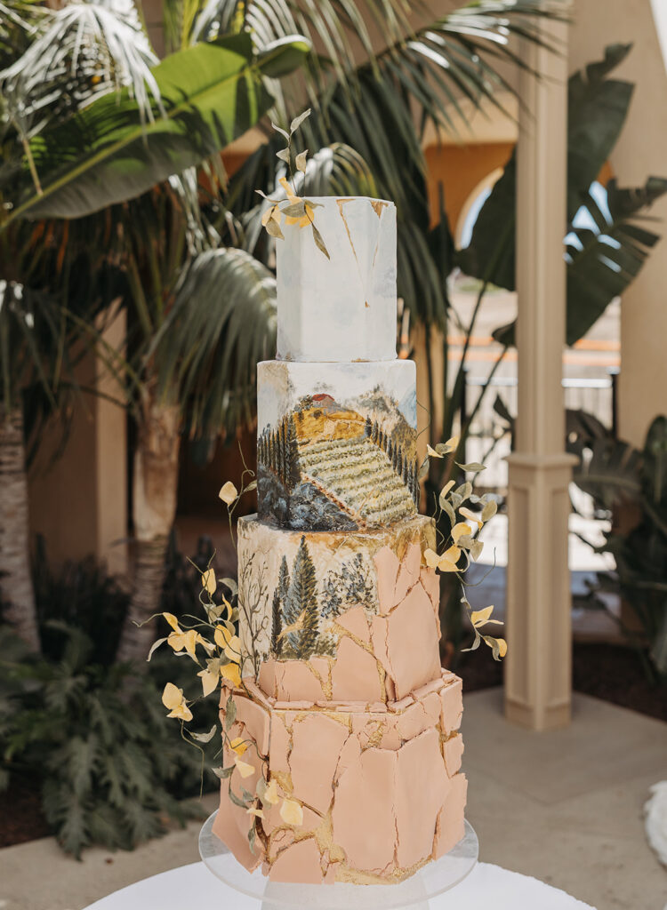 Textured multi-tier wedding cake with hand-painted landscape details and soft neutral tones, photographed during a Temecula wedding editorial in natural light.