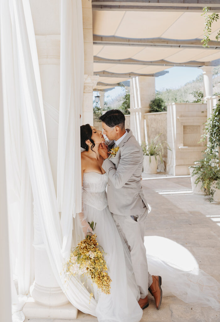 Bride and groom sharing an intimate moment beneath soft draping and stone columns during a Southern Bride editorial shoot in Temecula, California, captured in natural light.