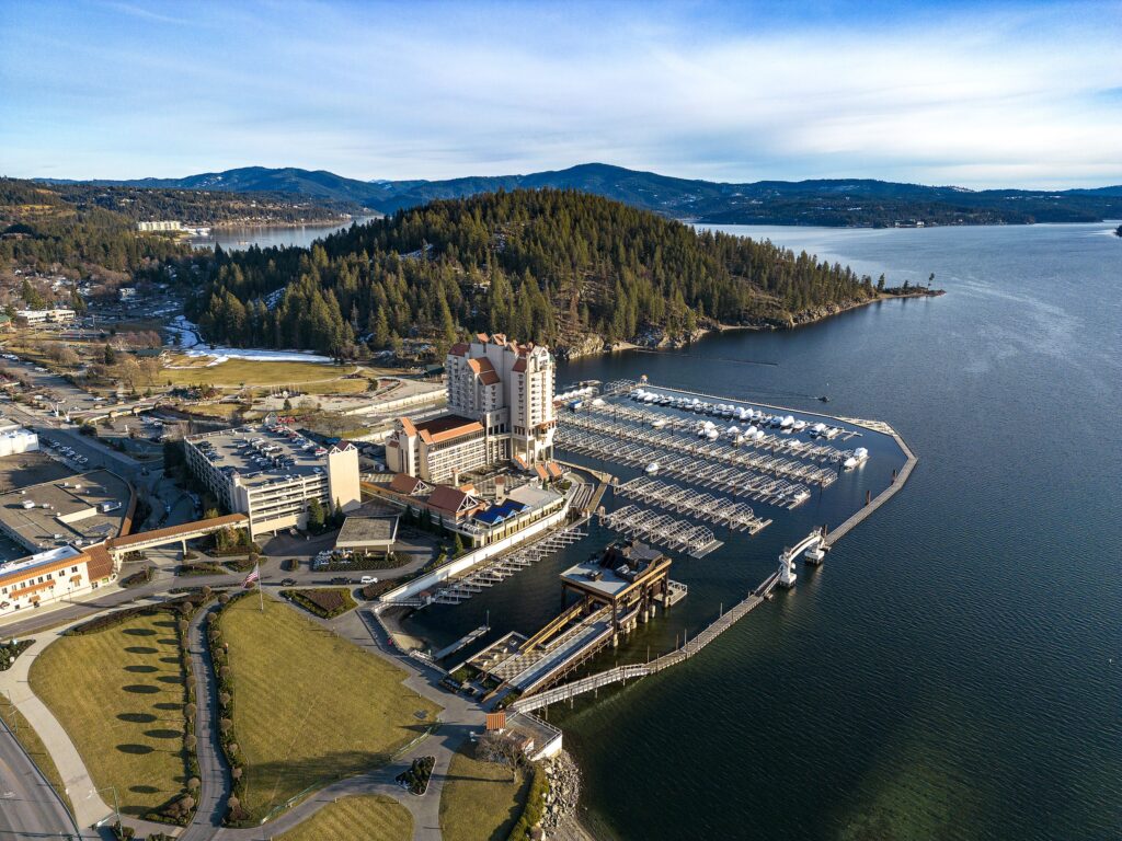 Aerial view of the CDA Resort on Lake Coeur d’Alene, showing the lakefront hotel, marina, and surrounding mountain landscape in Idaho