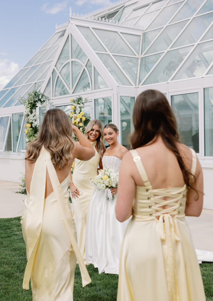 Bride takes photos with her bridesmaids in front of Greenhouse on Harvard